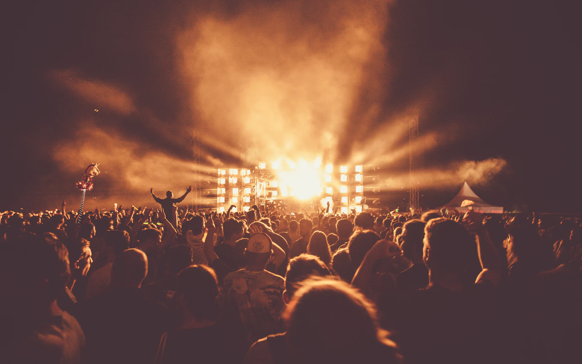 A packed crowd in front of a festival stage lit in warm gold.