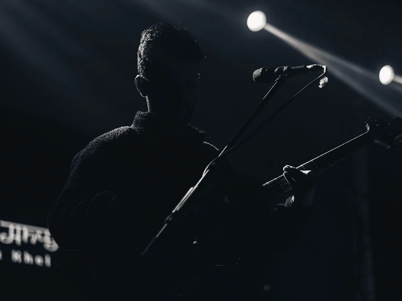 A guitarist in silhouette at a microphone under stage lights.
